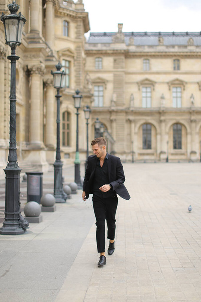 Young man walking near building in Paris, wearing black suit. - Zdjęcie, obraz
