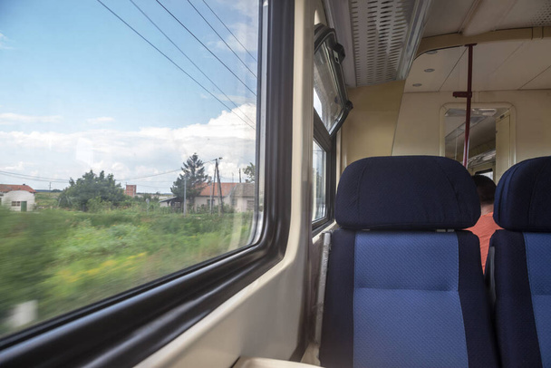 Lege stoelen in een moderne regionale trein, in Europese stijl, op een reis op het platteland met een snelheidsvervaging vanuit het raam - Foto, afbeelding