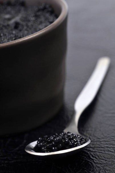 Spoon of caviar seen next to a ramekin close-up on a black background - Photo, image