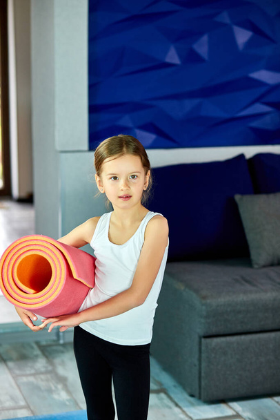 Egy kislány kezében fitnesz jóga rózsaszín szőnyeggel. Fitness egészséges és sport koncepció. Gyerekek sport otthon karantén. - Fotó, kép