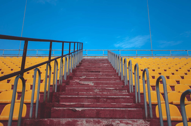 Stadyumdaki sarı sedlerin arasındaki kırmızı merdiven. - Fotoğraf, Görsel