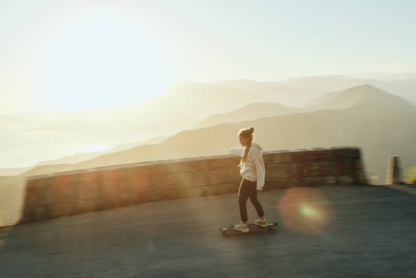 Young hipster woman with dreadlocks riding her long board down the mountain in beautiful scenic nature on road - Fotoğraf, Görsel