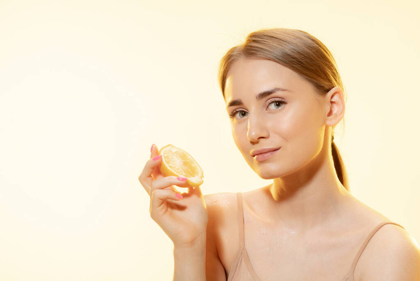 Citrus. Close up of beautiful female face with lemon slices over yellow background. Cosmetics and makeup, natural and eco treatment, skin care. - Zdjęcie, obraz