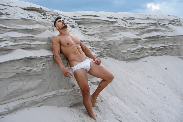 sexy mężczyzna, biały macho człowiek stojący w pobliżu wydm w seksownej pozie na tle niebieskiego nieba, kulturysta fitness oświetlone słońcem - Zdjęcie, obraz