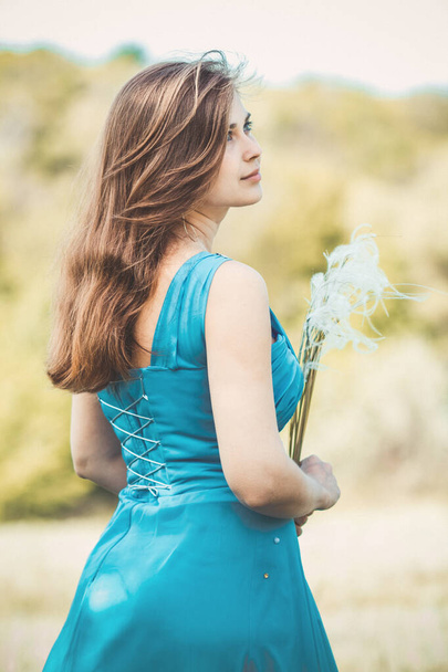 beautiful romantic girl enjoying nature with fluffy feather grass in hands, young elegant woman face, bride in blue long dress - Photo, Image
