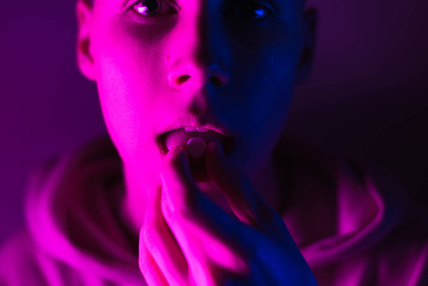 Junger Teenager im rosafarbenen Kapuzenpullover nimmt eine Droge in Tabletten. Zunge Kerl mit lsd Rad - Foto, Bild