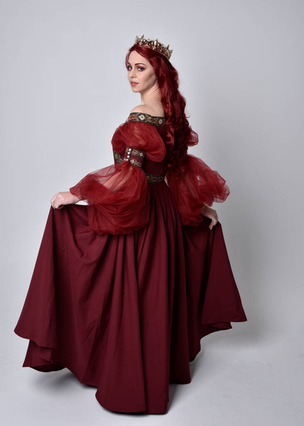 Portrét krásné ženy s rudými vlasy v rozevlátých burgundských fantasy šatech a zlaté koruně. celková délka stojící póza, izolovaná na pozadí studia - Fotografie, Obrázek