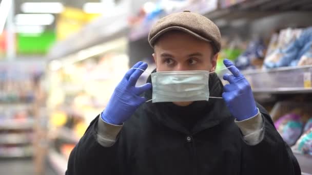 A young man in cap puts on a medical mask to protect against the epidemic, a close-up portrait in market. Protection from the coronavirus pandemic - Video