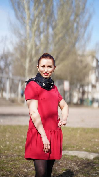Beautiful smiling woman in red dress in a park in spring. Woman posing and holding one hand on hip - Photo, Image