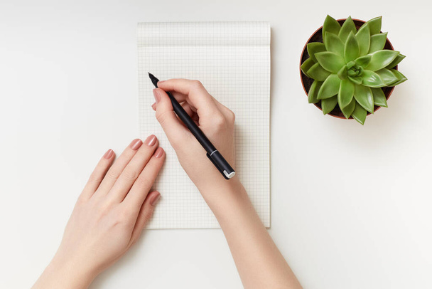 Επίπεδη lay των παχύσαρκων και γυναικών χέρια κρατώντας ένα στυλό πάνω από το σημειωματάριο χαρτί στο λευκό φόντο - Φωτογραφία, εικόνα