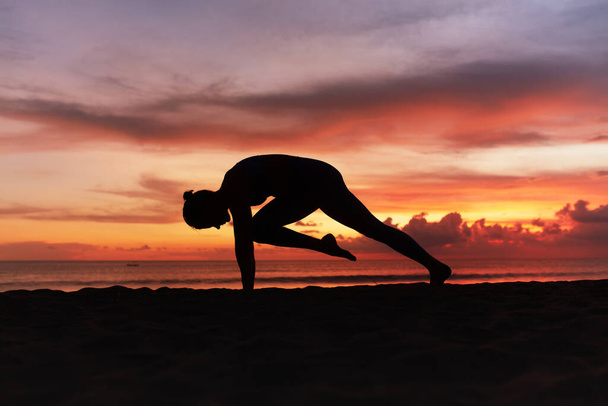 Yoga Poses. Woman Practicing Cat Stretch Asana On Ocean Beach. Female Silhouette Standing In Marjariasana Pose At Beautiful Sunset. Yoga As Exercise For Lifestyle. - Foto, Bild