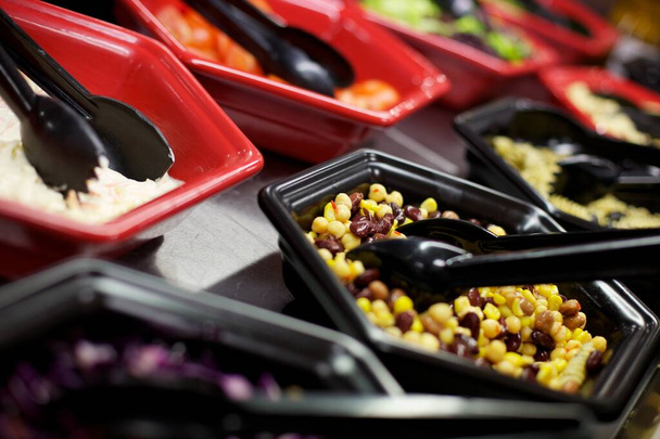 Insalatiere nere e rosse con pinze nere piene di diversi ingredienti per insalata
, - Foto, immagini