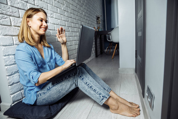 Beautiful business lady in casual is using a laptop and smiling while sitting on the floor at home and working - Foto, imagen