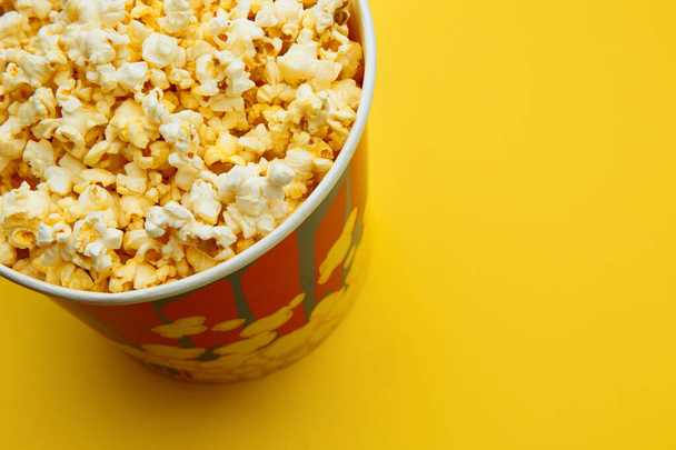 Popcorn in een kom op gele achtergrond, bovenaanzicht - Foto, afbeelding