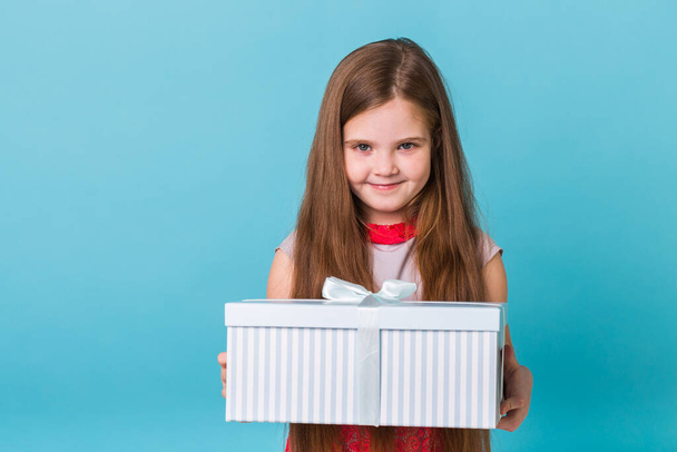 holidays, presents, christmas, childhood and birthday concept - smiling little girl with gift box over blue background - Foto, Imagem