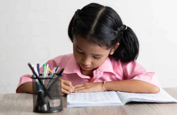 Маленька дівчинка робить домашнє завдання інтенсивно. Діти використовують жовтий олівець пише блокнот на дерев'яному столі. Виберіть неглибоку глибину фокусу з пробілом для копіювання на білому тлі
. - Фото, зображення