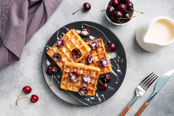 Belgian fluted waffles with fresh cherries and cream on a plate. Soft homemade waffles, sweet dessert with cherries - Φωτογραφία, εικόνα