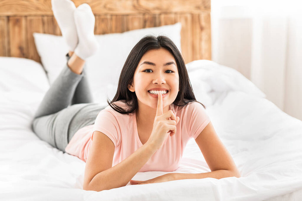 Ázsiai nő Gesturing Hush jel Feküdt az ágyon otthon - Fotó, kép
