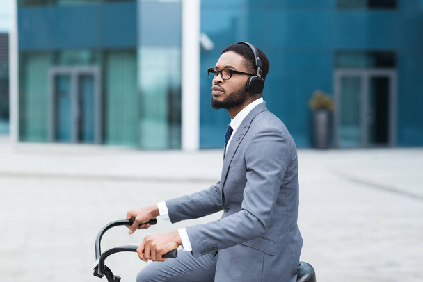 Black businessman in earphones riding on bike - 写真・画像