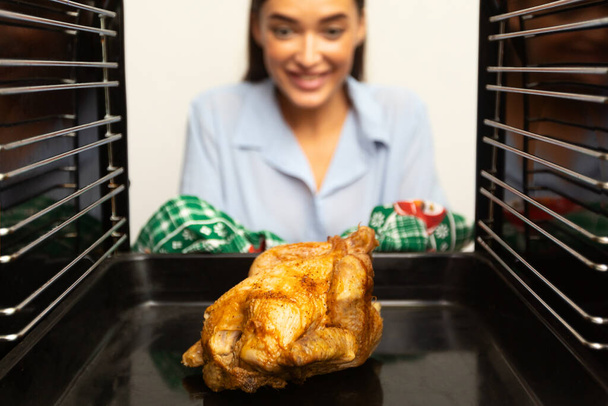 Uitzicht van binnenuit op geroosterde kip in oven en huisvrouw - Foto, afbeelding
