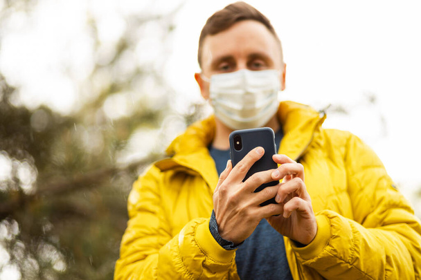 Man met chirurgisch masker houdt mobiele telefoon vast en maakt foto 's - Foto, afbeelding