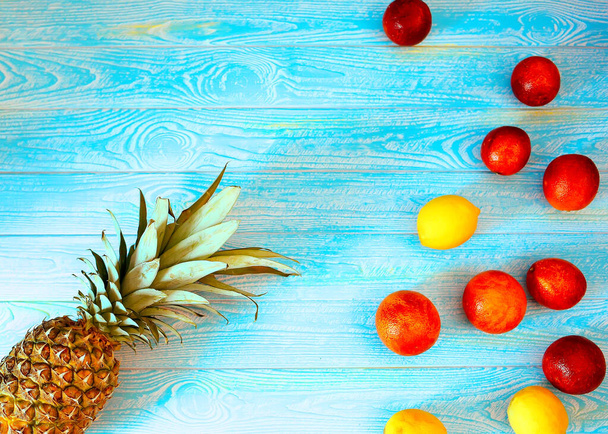 Mavi ahşap arka planda limonlu ananas ve kırmızı portakallar. Yaz kavramı. Meyve, eğlence ve turizm. - Fotoğraf, Görsel