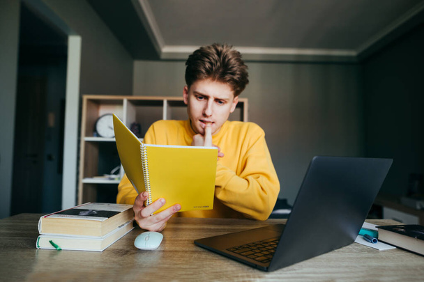 Soustřeď se na laptop. Mladý muž sedí doma u stolu, čte si zápisník a užívá si internet. Chytrý student studující doma na dálku. Karanténa. Pozadí. - Fotografie, Obrázek