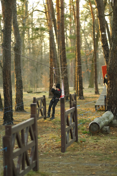 Portré egy fiúról, aki a levegőben repül a kötélen az őszi erdőben, biztonsági övet visel. - Fotó, kép
