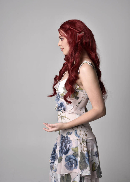 流れるような花のガウンを着て赤い髪を持つ美しい女性の肖像画。スタジオの背景に隔離された3/4ポーズ - 写真・画像