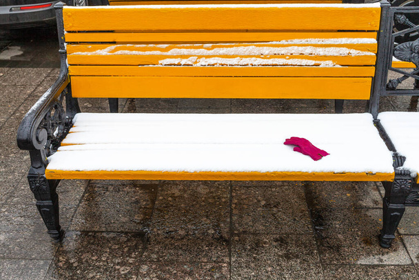 žlutá dřevěná lavička pokrytá sněhem s červenou ženskou rukavicí na Manezhnaya náměstí v Moskvě v zimě - Fotografie, Obrázek