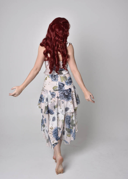 Muotokuva kaunis nainen punaiset hiukset yllään virtaava kukka puku. täyspitkä seisova asento, eristetty studion taustaa vasten
 - Valokuva, kuva