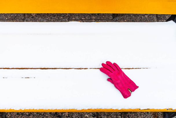 zapomniana czerwona rękawica damska na żółtej drewnianej ławce pokrytej śniegiem w zimie - Zdjęcie, obraz