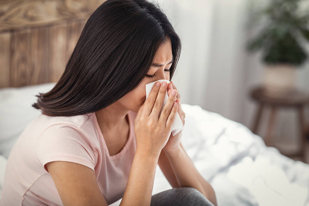 malade asiatique fille soufflage nez dans tissu assis dans chambre
 - Photo, image
