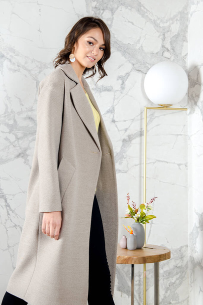 Beauty Fashion Model Girl with curls in light beige coat in a bright white loft style studio. Beautiful Luxury Winter Woman. Beauty and fashion. Spring and autumn clothes fashion Girl posing at studio - Φωτογραφία, εικόνα