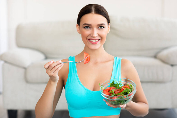 pasvorm dame eten groente salade glimlachen naar camera thuis - Foto, afbeelding