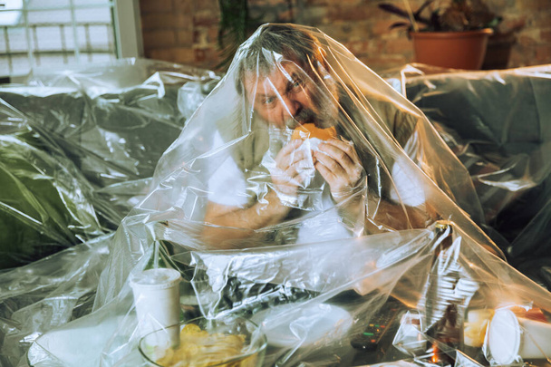 Senior man covered with plastic, eating fast food and drinking beer - environmental pollution by people concept - Fotografie, Obrázek