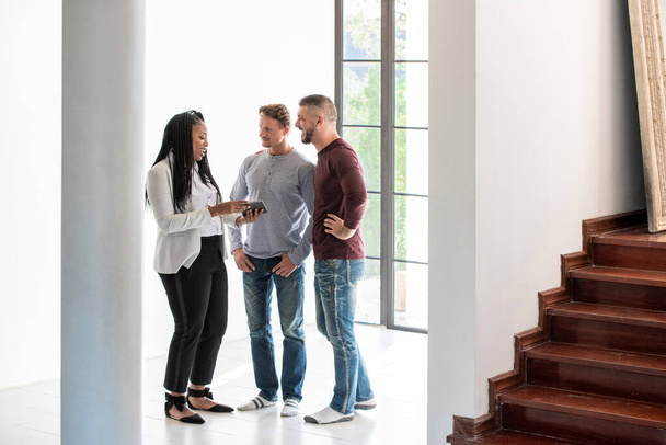 Feminino afro-americano agente imobiliário discutindo e dando informações para casal gay cliente em nova casa
 - Foto, Imagem