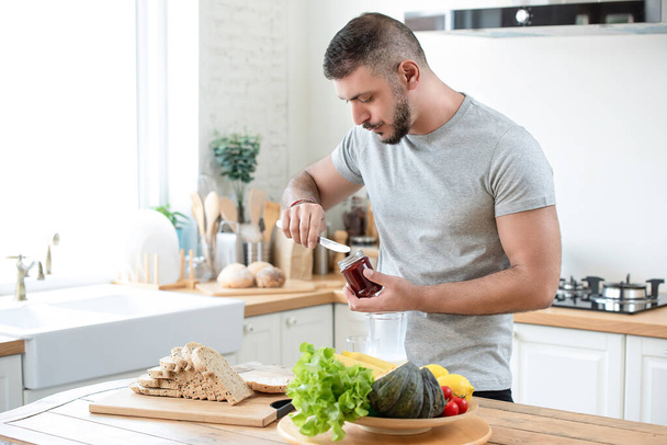 Mature fit bearded caucasian man preparing healthy breakfast sandwich in kitchen - Photo, Image