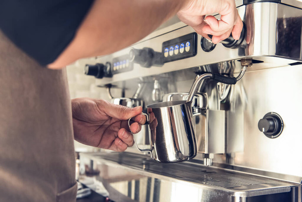 Kahve makinesiyle sütü buharda pişiren barista kafede latte sanatı yapmaya hazırlanıyor. - Fotoğraf, Görsel