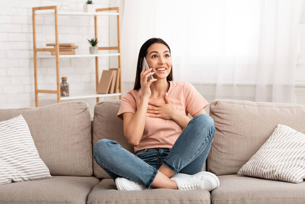 Excited woman talking on mobile phone sitting on couch - Φωτογραφία, εικόνα