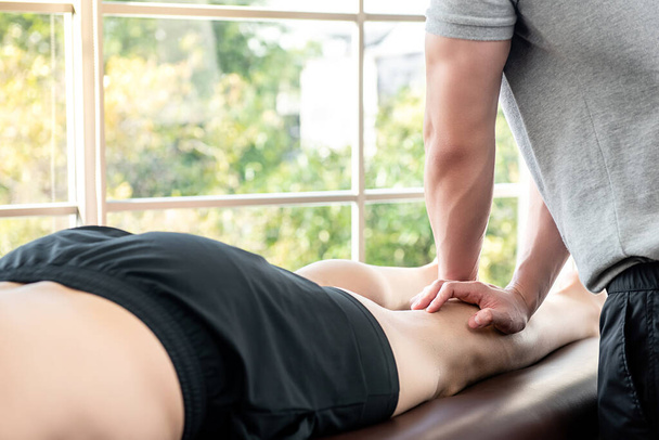 スポーツ理学療法の概念のための診療所のベッドの上のアスリートの患者に足とふくらはぎのマッサージを与える男性セラピスト - 写真・画像