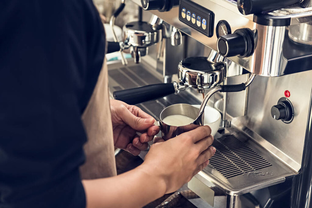 Barista leche humeante en la jarra con máquina de café preparándose para hacer arte de café con leche en la cafetería
 - Foto, Imagen