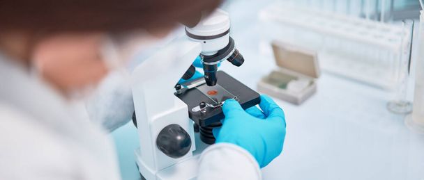 Primer plano de la mujer asistente de laboratorio en guantes de goma azul mirando a través del microscopio
. - Foto, imagen