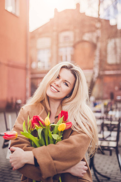 Skandináv szőke tavasszal virágokkal - vonzó lány örül a tavaszi napsütésnek és melegszik a hosszú tél után - Fotó, kép