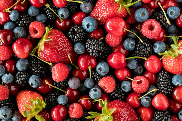 Una vista horizontal de arriba hacia abajo de una variedad de bayas maduras, incluyendo fresas, arándanos y cerezas
. - Foto, imagen