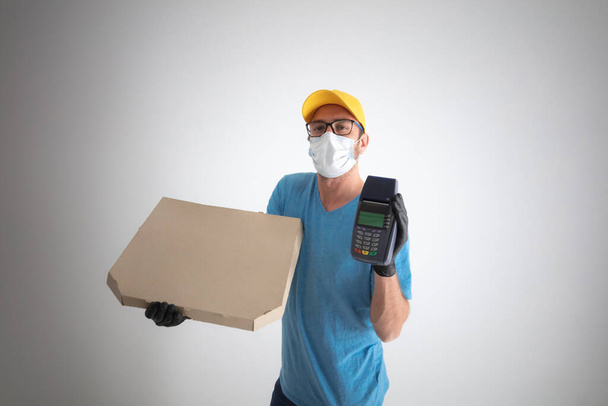 Livraison gars avec masque de protection tenant boîte à pizza et POS pour le paiement sans contact
. - Photo, image