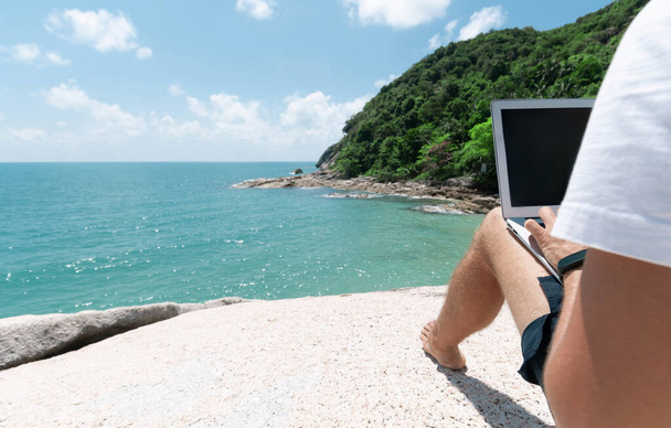 Young man freelancer works remotely on a high coastal cliff overlooking the Gulf of Thailand. - Photo, Image