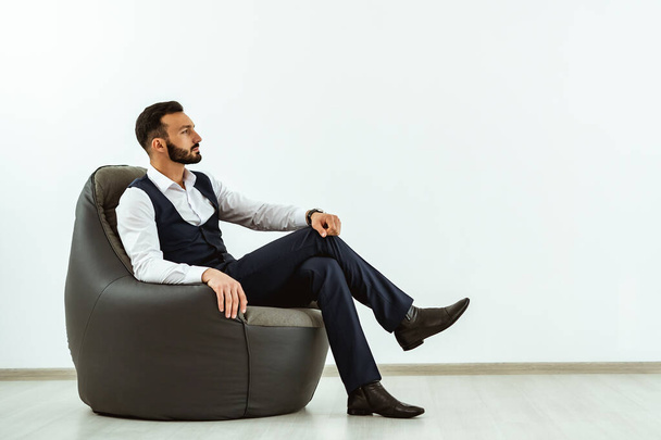 El hombre de negocios sentado en una silla bolsa en el fondo blanco de la pared
 - Foto, Imagen