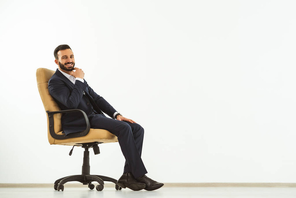 El hombre feliz sentado en una silla de oficina en el fondo blanco de la pared
 - Foto, imagen