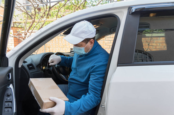 保護手袋とマスクの宅配業者は、段ボール箱、顧客へのオンライン注文の配達で車から出てきます。安全な配送コンセプト。危険なウイルスに対する保護措置. - 写真・画像